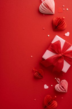 Kırmızı bir fiyonk ve kalp şeklindeki süslemelerle süslenmiş bir hediye içeren bayramlık sevgililer günü dikey kompozisyonu. Sevgi ve sevgiyi kutlamak için mükemmel.