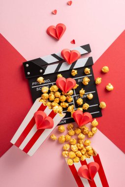 Kırmızı ve pembe arkaplanda kağıt kalplerle düzenlenmiş patlamış mısır dikey kutusu ve el çırpma tahtası, romantizmi ve filmi simgeliyor.