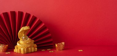 Kırmızı arka planda, Çin Yeni Yılı 2025 'i simgeleyen kağıt yelpazeli altın yılan süsü. Ay takvimini geleneksel renkler ve kültürel unsurlarla kutlamak için mükemmel.