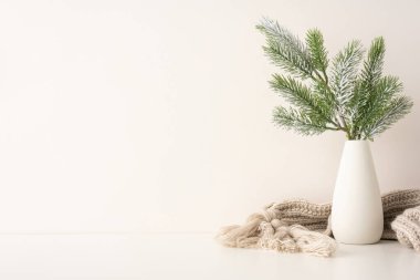 Beyaz bir vazoda çam dalları bulunan basit, zarif İskandinav esinlenilmiş bir kış manzarası. Yumuşak, nötr renkler rahat bir atmosfer yaratıyor. Tatil ve Noel süslemeleri için mükemmel.