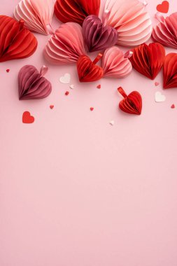 Pembe bir yüzeydeki kalp şeklinde dikey kağıt süslemeler el yapımı bir dokunuşla romantik bir Sevgililer Günü atmosferi yaratır.