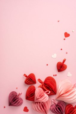 Kırmızı ve pembe kağıt kalplerden oluşan dikey bir koleksiyon pembe arka planda güzelce düzenlenmiş, Sevgililer Günü için aşkı ve aşkı simgeliyor.