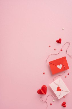 Pembe arka plana yerleştirilmiş kalp kesikleri olan kırmızı ve beyaz dikey zarflar sevgi ve sevgiyi simgeliyor. Sevgililer Günü temaları için ideal
