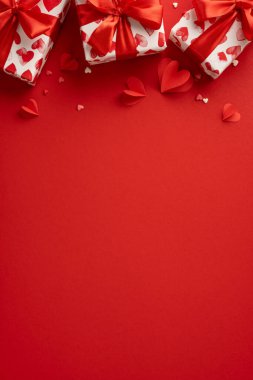 Romantik Sevgililer Günü dikey sahnesinde arka planda kırmızı kurdeleli kalp desenli hediye kutuları var.