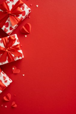 Güzel sarılmış dikey sevgililer günü hediyeleri, canlı kırmızı bir yüzey üzerinde kalp desenleri ve kurdeleler romantik bir sahne oluşturur. Sevgililer Günü 'nde sevgi ve sevgiyi kutlamak için ideal.