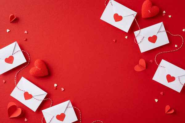 Верхний вид чистых красных конвертов, украшенных бумажными сердцами и украшениями на ярком красном фоне. Перфект ко Дню святого Валентина или романтическим событиям.