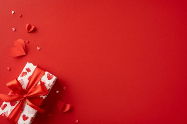 Kırmızı kalpler ve kurdelelerle süslenmiş güzel paketlenmiş bir hediye kutusu, kırmızı bir arkaplanda duruyor. Sevgililer Günü kutlamaları ve romantik kutlamalar için mükemmel.