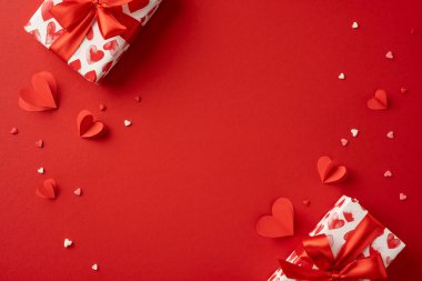 Güzel bir Sevgililer Günü sahnesi, hediye kutuları ve kırmızı arka planda kalp süslemeleri. Aşkı kutlamak ve romantik duyguları düşünceli hediyelerle ifade etmek için mükemmel.