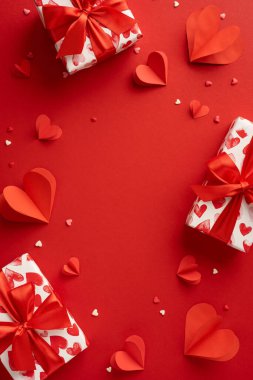 Güzelce paketlenmiş hediyeler ve canlı kırmızı kağıt kalplerle romantik ve şenlikli bir atmosfer yaratan dikey ve çarpıcı bir Sevgililer Günü düzenlemesi.