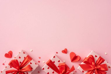 Sevgililer Günü hediyeleri kırmızı kurdeleye sarılı pembe bir yüzey üzerinde kalp süslemeleri