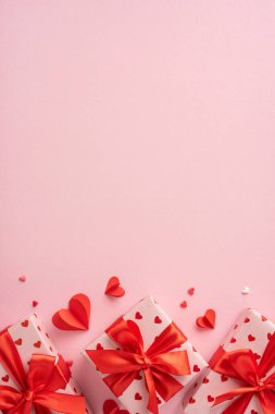 Dikey sevgililer günü hediyeleri kalp desenli kağıt ve kırmızı kurdelelerle sarılmış, kağıt kalplerle çevrili, romantik bir ortam yaratıyor.