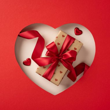 Güzel paketlenmiş bir Sevgililer Günü hediyesi. Kırmızı bir arka planda kırmızı bir kurdele var. Aşkı ve romantizmi simgeliyor.