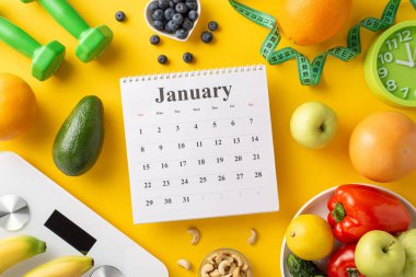 Ocak ayında, yeni yıla sağlıklı bir başlangıç ve dengeli diyet kavramını simgeleyen taze meyve, sebze ve fitness ürünleriyle çevrili bir takvim.