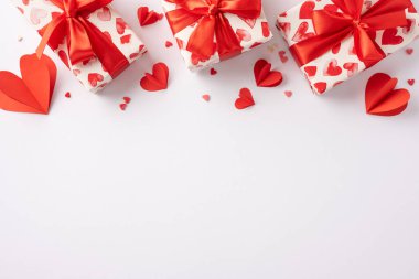 Kalp desenli kağıt ve kırmızı kurdelelerle kaplanmış, kağıt kalplerle çevrili hediyelerin üst görüntüsü. Sevgililer Günü kutlamaları ve hediye kutlaması için mükemmel.