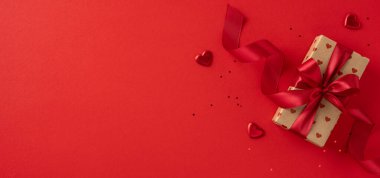 Güzel paketlenmiş kırmızı kurdeleli bir hediye kutusu, kalp süslemeleriyle çevrili kırmızı bir arka planda oturur. Sevgililer Günü kutlamaları, romantizm ve aşk temalı etkinlikler için mükemmel..