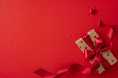 Kırmızı kurdeleli güzel bir hediye ve canlı kırmızı arka planda kalp süslemeleri, Sevgililer Günü için mükemmel. Sahne aşkı, romantizmi ve kutlamayı çağrıştırıyor.