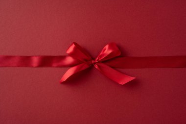 Parlak kırmızı kurdele, canlı kırmızı bir arka plana zarif bir şekilde bağlanmış. Sevgililer Günü temalarını, aşkı, romantizmi ve kutlamayı simgeliyor.