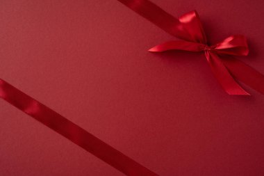 Koyu kırmızı bir yüzeye, sevgi ve zarafeti sembolize eden canlı kırmızı bir kurdele. Bu minimalist görüntü Sevgililer Günü, hediye verme ya da romantik temalar için mükemmel.