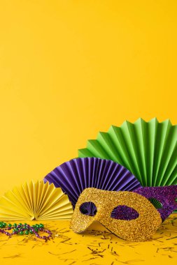 Mardi Gras yan dikey görünüm temalı kurulum parlak altın bir maske, renkli boncuklar ve parlak sarı bir arka plana karşı kağıt yelpaze