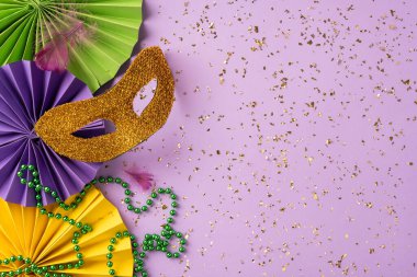Parlak ve dekoratif maske ve boncuklar parlak mor bir zemin üzerine yerleştirilmiş altın parıltılar Mardi Gras cazibesini vurguluyor.