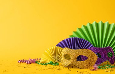 Mardi Gras kutlamaları için yeşil ve sarı kağıt yelpazeli altın ve mor parıltılı maskelerin yan görüntüsü
