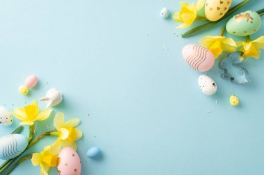 Mavi bir yüzey üzerinde pastel renkli yumurtalar ve sarı çiçekler içeren Paskalya temalı düzenleme
