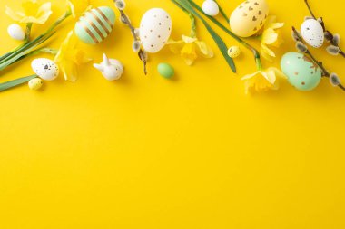 Süslü yumurtalar, nergisler ve parlak sarı bir zemin üzerinde yaratıcı bir şekilde düzenlenmiş küçük tavşan heykelciğinin yer aldığı Paskalya kompozisyonu