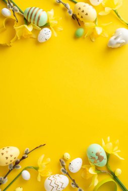 Parlak Paskalya yumurtaları, çiçekler ve parlak sarı dikey arka planda sergilenen dekorasyonlar. Tatil, bahar ve festival temaları için mükemmel.