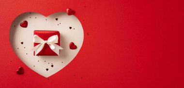 Küçük kalplerle çevrili, içinde bir kurdele bulunan kırmızı bir hediye kutusu. Aşk ve kutlama duyguları yakalıyor.