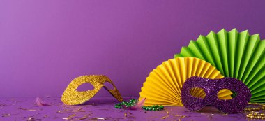 Mardi Gras yan görünüm aksesuarları arasında simli maskeler ve mor arkaplandaki şenlikli dekorasyonlar da var