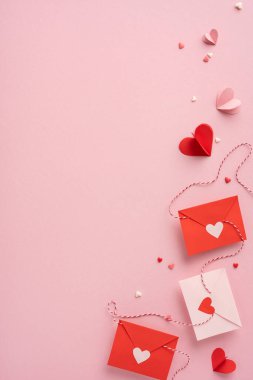 Pembe arka plana yerleştirilmiş kalp kesikleri olan kırmızı ve beyaz dikey zarflar sevgi ve sevgiyi simgeliyor. Sevgililer Günü temaları için ideal