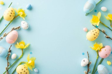 Renkli boyalı Paskalya yumurtaları ve taze sarı çiçekler yumuşak mavi bir arkaplan çerçevesi.
