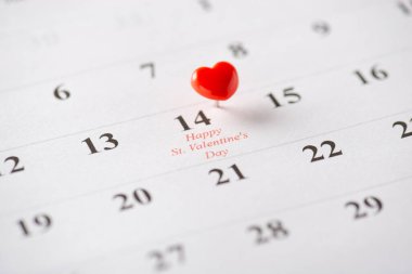 A small red heart-shaped pin marking Valentine's Day on a calendar page, symbolizing love clipart