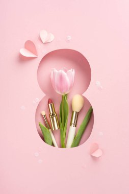 Pembe dikey lale makyaj fırçaları ve pembe bir arka planda ruj ile çevrili.