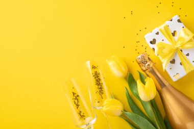 Taze sarı laleler, köpüklü şampanya şişesi, şenlikli hediyeler ve neşeli sarı arka plandaki kadehler neşeyi kutluyor, hediyeler veriyor, aşk ve mutluluğu.