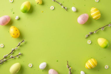 Neşeli desenli Paskalya yumurtaları, çiçekli elementler ve yeşil bir yüzeyde sergilenen dallar.