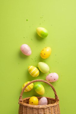 Dekoratif dikey sarı, yeşil ve pembe paskalya yumurtaları hasır bir sepetle güzelce şekillendirilmiş. Bahar geleneklerini ve canlı mevsimsel estetiği kutlar.