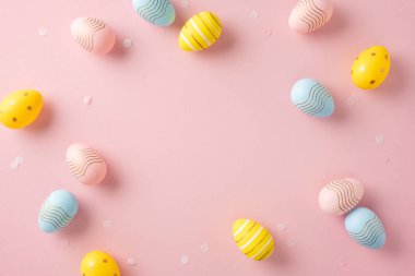 Dekoratif Paskalya yumurtaları yaratıcı bir düzende yumuşak pembe bir zeminde sergilenir.