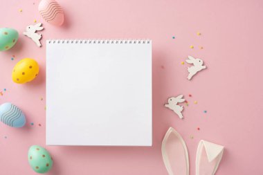 Paskalya düz kompozisyonu, içi boş bir not defteri ile çevrili pembe arka planda neşeli yumurta ve tavşan süslemeleri, festival ve mevsimlik temalar için mükemmel.