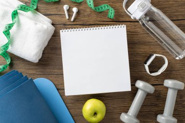 Bir defter, halterler, su şişesi ve mezura da dahil olmak üzere spor malzemelerinin düzlüğü.