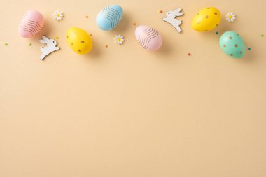 Çiçekli ve tavşan desenli dekoratif Paskalya yumurtaları bej bir yüzeyde yaratıcı bir şekilde dizilmiş.