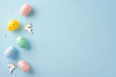 Renkli Paskalya yumurtaları ve ahşap tavşan heykelcikleri pastel mavisi üzerinde ustalıkla sergileniyor.