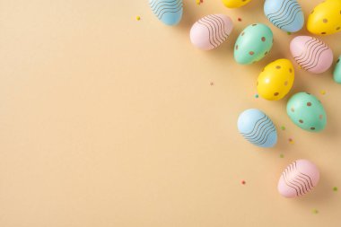 Renkli, dikey dekore edilmiş Paskalya yumurtaları pastel renkli bir yüzeye saçılmış ve neşeli bir hava katıyor.
