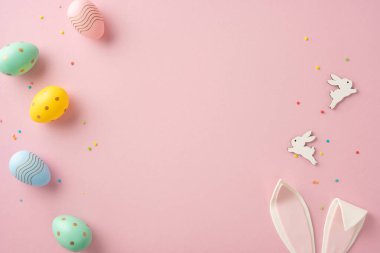 Boyalı Paskalya yumurtaları, dekoratif tavşan figürleri ve pembe arka planda renkli konfetilerin yer aldığı şenlikli bir düzen.