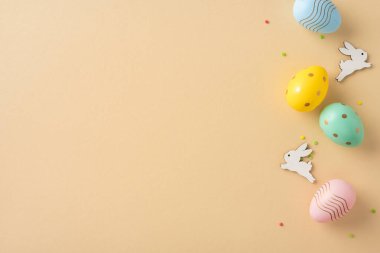 Sarı ahşap süsler ve renkli Paskalya yumurtaları bej arka planda güzelce dizilmiş.