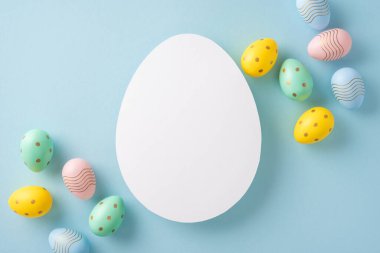 Yumuşak mavi arka planda canlı, dekoratif yumurtalarla çevrili boş yumurta şekilli Paskalya konsepti, kutlama ve karşılama tasarımları için ideal.