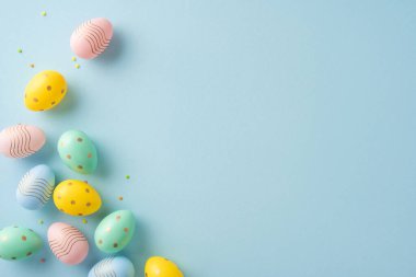 Renkli Paskalya yumurtaları. Pastel mavi bir yüzeye saçılmış desenleri var. Kompozisyon, neşeli ve neşeli bir Paskalya kutlamasının havasını çağrıştırıyor.