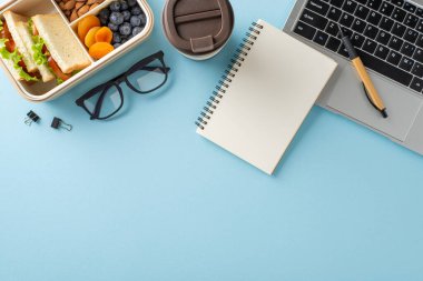 Mavi çalışma alanı üzerinde sağlıklı atıştırmalıklar, kahve, defter ve bardaklarla dolu Bento kutusu.