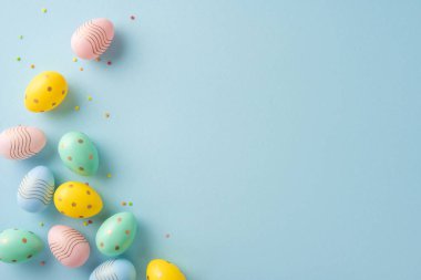 Pastel renginde paskalya yumurtaları, dekoratif tasarımlarıyla birlikte yumuşak bir arka planda, bayram havası vermek için dağınık küçük konfetiler eşliğinde.