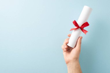 Kırmızı kurdeleyle bağlanmış, başarıyı ve eğitimi simgeleyen yuvarlak diplomayı sunan bir el.